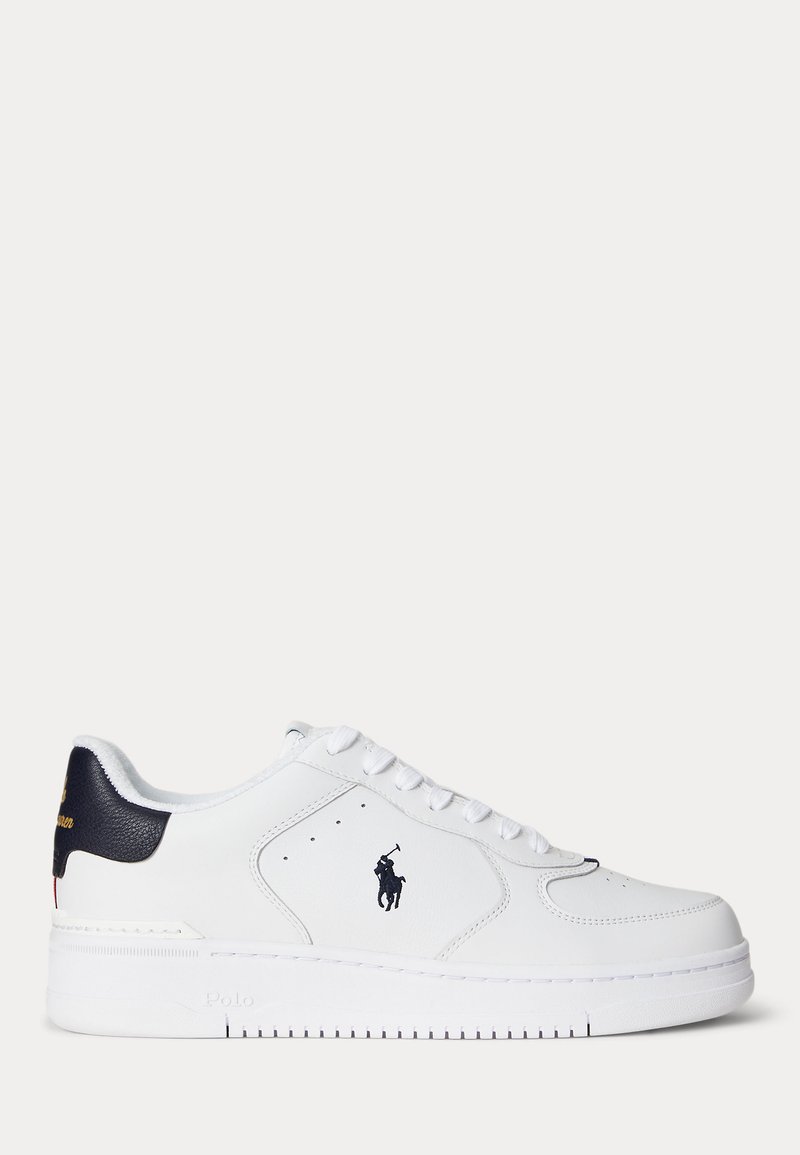 Λευκό sneaker χαμηλού προφίλ με ναυτικό ταμπελάκι στη φτέρνα, μαύρο λογότυπο παίκτη πόλο στο πλάι και λευκά κορδόνια σε απλό φόντο.