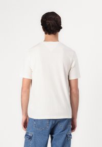 White short-sleeve t-shirt with a subtle v-shaped design at the back, paired with light blue cargo jeans, showcasing a casual fit.
