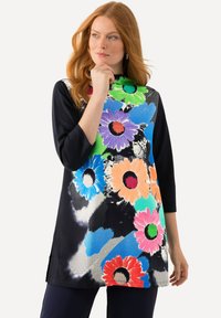 Eine farbenfrohe Tunika mit großen Blumenmustern in Grün, Blau, Lila und Orange auf schwarzem Hintergrund, mit einem Stehkragen und drei Viertelärmeln.