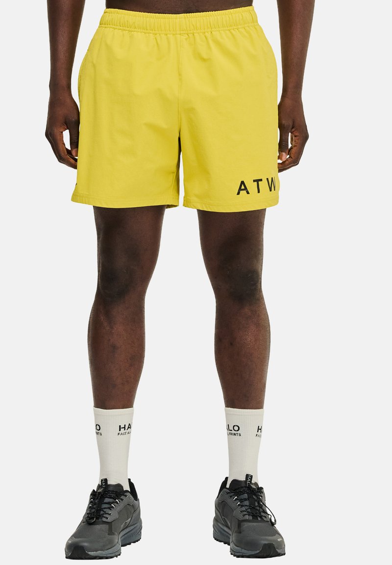 Gula shorts med elastisk midja, med en sidologotyp "ATW" i svart. Bärs med svarta sneakers och vita strumpor.