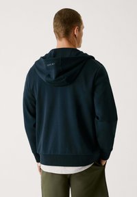 Marineblaues Hoodie mit normaler Passform, ausgestattet mit einer doppellagigen Kapuze und Logo-Text auf dem Rücken. Weicher Stoff und gerippte Bündchen.