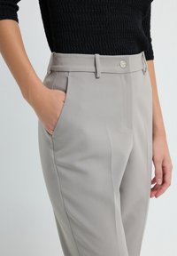 Light gray tailored trousers with a smooth texture, featuring a flat front, belt loops, and side pockets. Silver button detail on waistband.