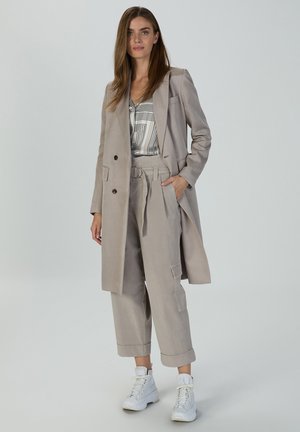Light gray, tailored coat over a striped blouse, complemented by loose gray trousers with a belt. White sneakers complete the outfit.