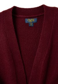 Burgunderfarbene Kinder-Strickjacke mit V-Ausschnitt, aus weichem, strukturiertem Stoff gefertigt. Mit einem Etikett, das die Größe 4-5 Jahre angibt.