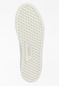Semelle de chaussure blanche avec un motif diamant texturé et le logo embossé "GUESS" près du talon, conçue pour la traction et la stabilité.