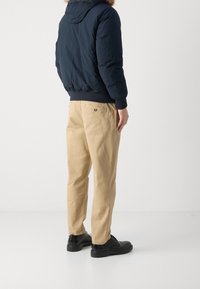 Marineblauwe gewatteerde jas met capuchon, elastische manchetten, gecombineerd met beige chinos. Zwarte schoenen maken de outfit compleet. De achterkant toont een eenvoudig ontwerp.