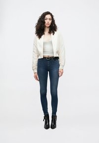 Fehér rövid bomberdzseki szürke felsővel, sötétkék szűk farmernadrággal és fekete bokacsizmával, fekete övvel párosítva.