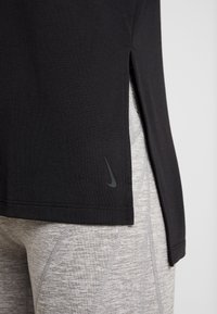 Camiseta deportiva negra con aberturas laterales, con un discreto logo gris de Nike en el dobladillo, combinada con leggings de textura gris claro.