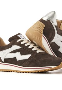 Baskets en daim marron avec des accents en cuir blanc, lacets ronds et une semelle en caoutchouc texturé. Présentent un détail de talon métallique argenté et des rayures contrastantes.