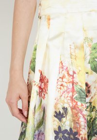 Falda de estampado floral en tejido ligero con pliegues, que presenta patrones rojos, violetas y verdes sobre un fondo blanco y amarillo.