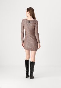 Vestido de malha castanho brilhante com mangas longas, bainha canelada e decote largo, combinado com botas pretas de salto alto até ao joelho.