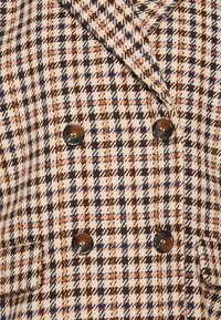 Cappotto doppiopetto con un motivo a pied de poule nei colori marrone, arancione e blu navy, con bottoni lucidi neri e un tessuto strutturato intrecciato.