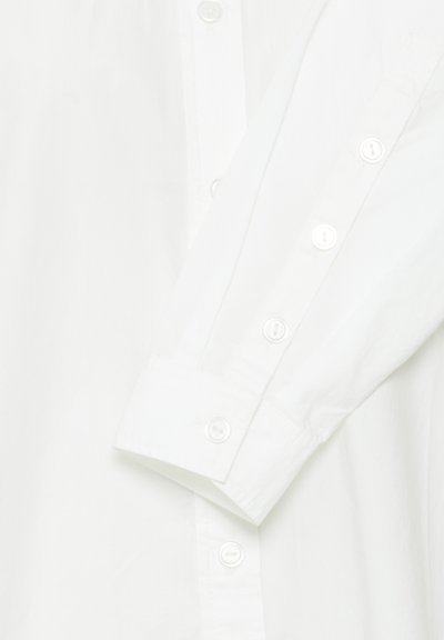 Balta mygtukų marškiniai su ilgomis rankovėmis, pasižymintys lygiu medvilnės audiniu ir baltomis mygtukais palei praktiškumą ir rankogalius.