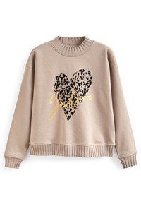 Sudadera beige con cuello y puños acanalados. Presenta un corazón con estampado de leopardo negro y texto dorado "J’adore" en el centro.
