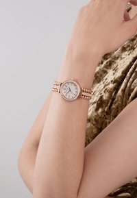 Różowe złoto zegarek na rękę z okrągłą białą tarcz�ą, ozdobioną cyrkoniami, oraz teksturowaną metalową bransoletą z ogniwami i zapięciem.