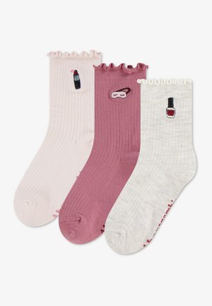 Trois chaussettes côtelées avec des hauts froncés en rose, mauve et crème, chacune brodée avec des icônes de maquillage : rouge à lèvres, masque de sommeil et vernis à ongles.