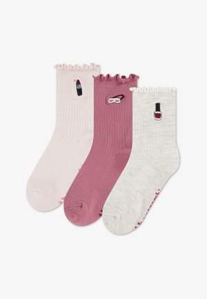 Trois chaussettes côtelées avec des hauts froncés en rose, mauve et crème, chacune brodée avec des icônes de maquillage : rouge à lèvres, masque de sommeil et vernis à ongles.