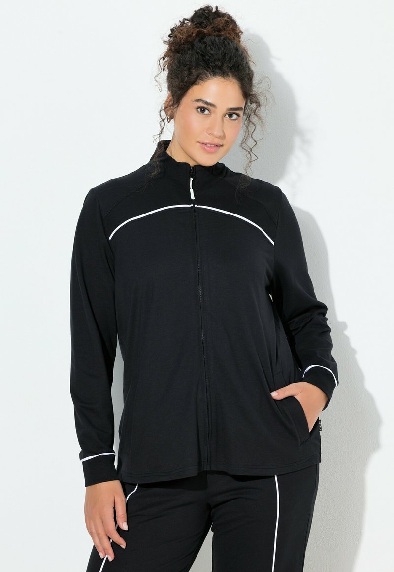 Schwarze Reißverschlussjacke mit hohem Kragen, ausgestattet mit weißen Paspelierungen entlang der Nähte. Hergestellt aus glattem Stoff, verfügt sie über Seitentaschen und lange Ärmel.