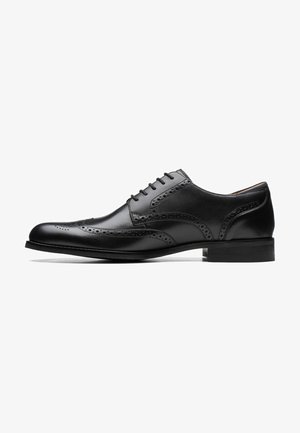 Black leather dress shoe with brogue detailing, smooth texture, rounded toe, flat heel, and classic lace-up design.