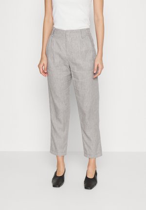 Femme portant un pantalon gris clair taille haute, court et droit, avec un haut blanc sans manches et des chaussures noires à bout carré.