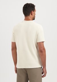 Korte mouwen beige getextureerd t-shirt met een subtiel ruitpatroon, ronde halslijn en een rechte zoom. Draag met lichtgekleurde broeken.