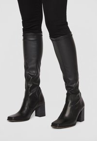 Bottes noires en cuir jusqu'au genou avec un talon carré, présentant un design élégant, une texture lisse et un bout carré.
