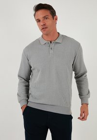 Sweatshirt polo gri cu dungi, cu mâneci lungi, guler polo și plasă cu două nasturi. Prezintă un material texturat și un design ajustat.