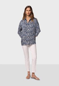 Camicia a collare blu e bianca a fantasia con maniche lunghe, abbinata a pantaloni bianchi slim-fit e sandali di colore argento. Tessuto dalla texture liscia.