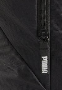 Schwarzer Stoffrucksack mit strukturierter Oberfläche, einem Reißverschluss und einem schwarzen Etikett mit "PUMA" in weißer Schrift.