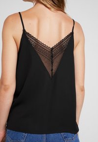 Camisole noire avec un dos en dentelle en V, des bretelles fines et des accents de boutons. Matériau lisse avec une coupe décontractée.