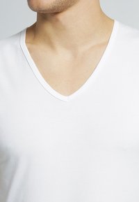 T-shirt bianco in cotone con scollo a V, dalla texture liscia, design aderente, con un taglio del collo sottile, senza motivi o accenti visibili.