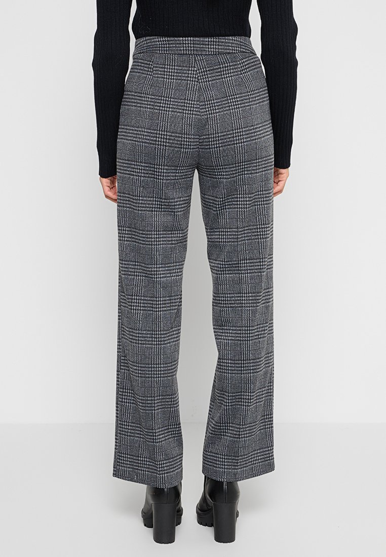 Graue karierte High-Waist-Hosen mit weitem Bein und strukturierter Stoffbeschaffenheit. Sie verfügen über ein dezentes Karomuster und werden mit einem schwarzen gerippten Pullover kombiniert.