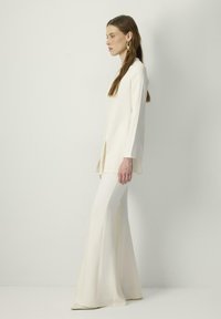 White long-sleeve top with side slits paired with flared white pants. Smooth fabric texture, minimalist design, showcasing a monochromatic look.