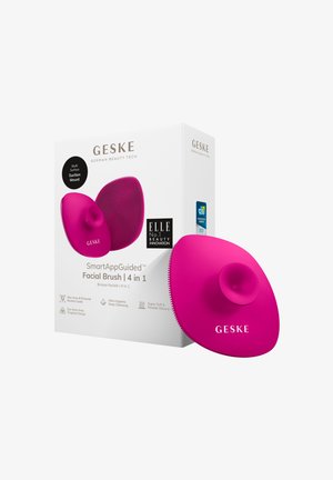 Bright pink silicone facial brush with a central suction mount, textured surface, and ergonomic shape. Box features product details and branding.