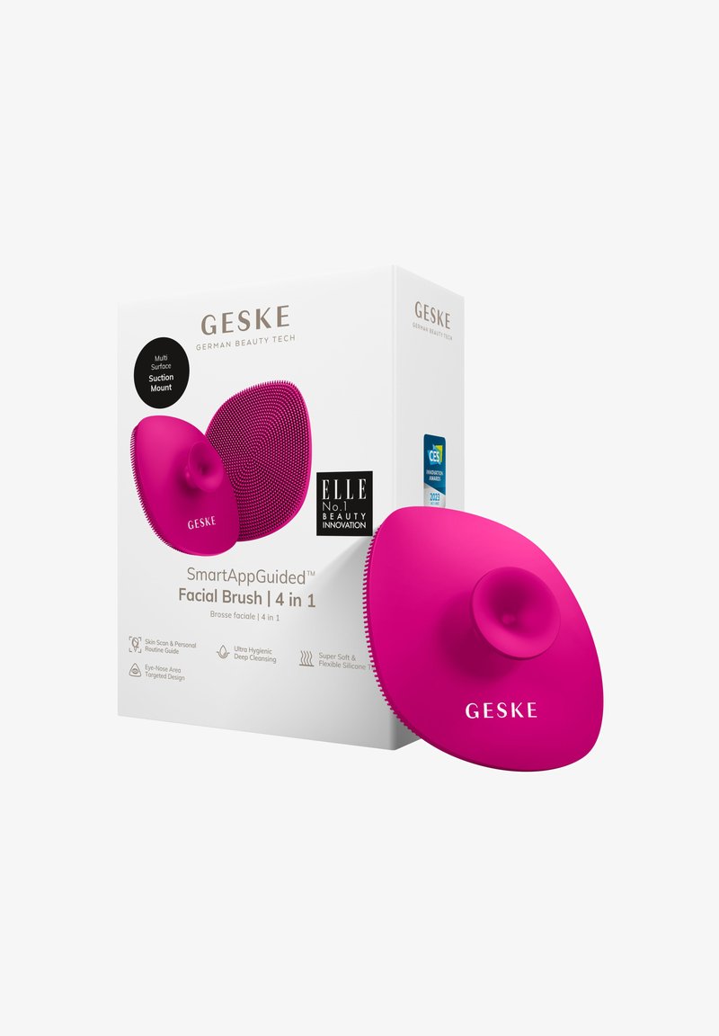 Helle rosa Silikon-Gesichtsborste mit einer zentralen Saugnapf-Befestigung, strukturierten Oberflächen und ergonomischer Form. Die Verpackung enthält Produktdetails und Branding.