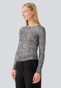 Long-sleeve black top with silver sparkles, made from a sheer material. Round neckline and fitted silhouette. Paired with black pants.