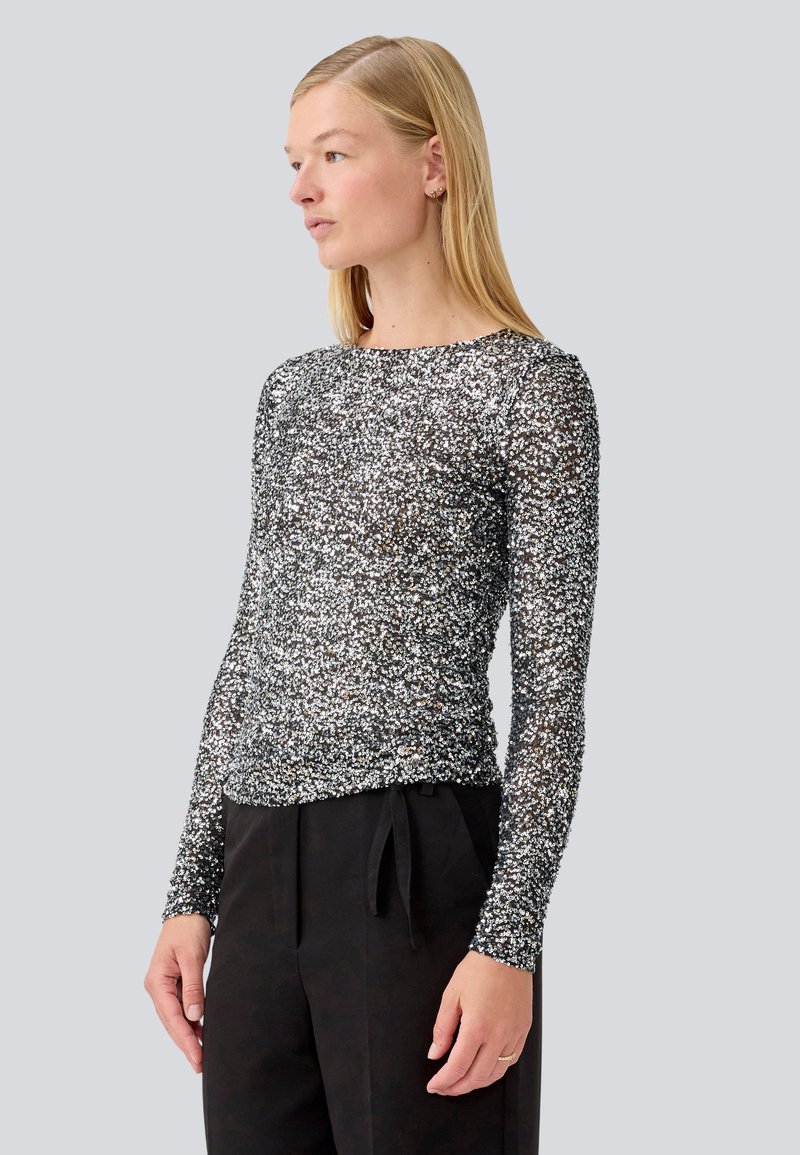 Long-sleeve black top with silver sparkles, made from a sheer material. Round neckline and fitted silhouette. Paired with black pants.