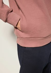 Sudadera texturizada en color rosa con puños y dobladillo acanalados, combinada con pantalones de un azul marino oscuro. La sudadera tiene un corte holgado y un detalle de bolsillo lateral.