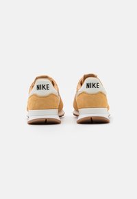 Nike-sneakers med en beige mockaövre, vita accenter och en gummisula. Har Nike-logotypen tydligt på hälen.