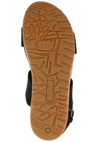 Musta sandaali, jossa on textured musta hihna, kumipohjalla, jossa on ruskea, kuvioitu uritus ja Timberland-logo.