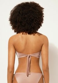 Bikiniöverdel utan axelband i ljusrosa tyg, med en knut bak. Slät textur med en minimalistisk design.