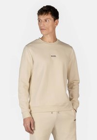 Pullover beige a girocollo realizzato in tessuto liscio, con un piccolo logo nero centrato sul petto, maniche lunghe e polsini a costine.