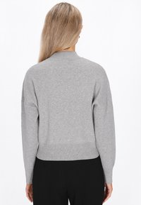 Grauer Strickpullover mit rundem Ausschnitt, gesenkten Schultern und geripptem Saum. Die Textur wirkt weich und die Passform ist leger.