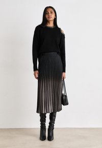 Μαύρος πλεκτός πουλόβερ με κόψιμο στους ώμους και κολιέ από χάντρες; αναδιπλωμένη φούσ�τα μαύρου-γκρι ombre; μαύρες μπότες μέχρι το γόνατο; μαύρη τσάντα.