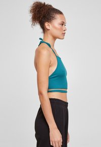 Teal ribbet crop top med spaghetti stropper, med en tettsittende design og en rå kant. Kombinert med svarte bukser med elastisk midje.