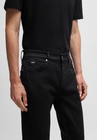 Black denim jeans with a straight cut, featuring contrast stitching, metal hardware, and a small brand label on the back pocket.