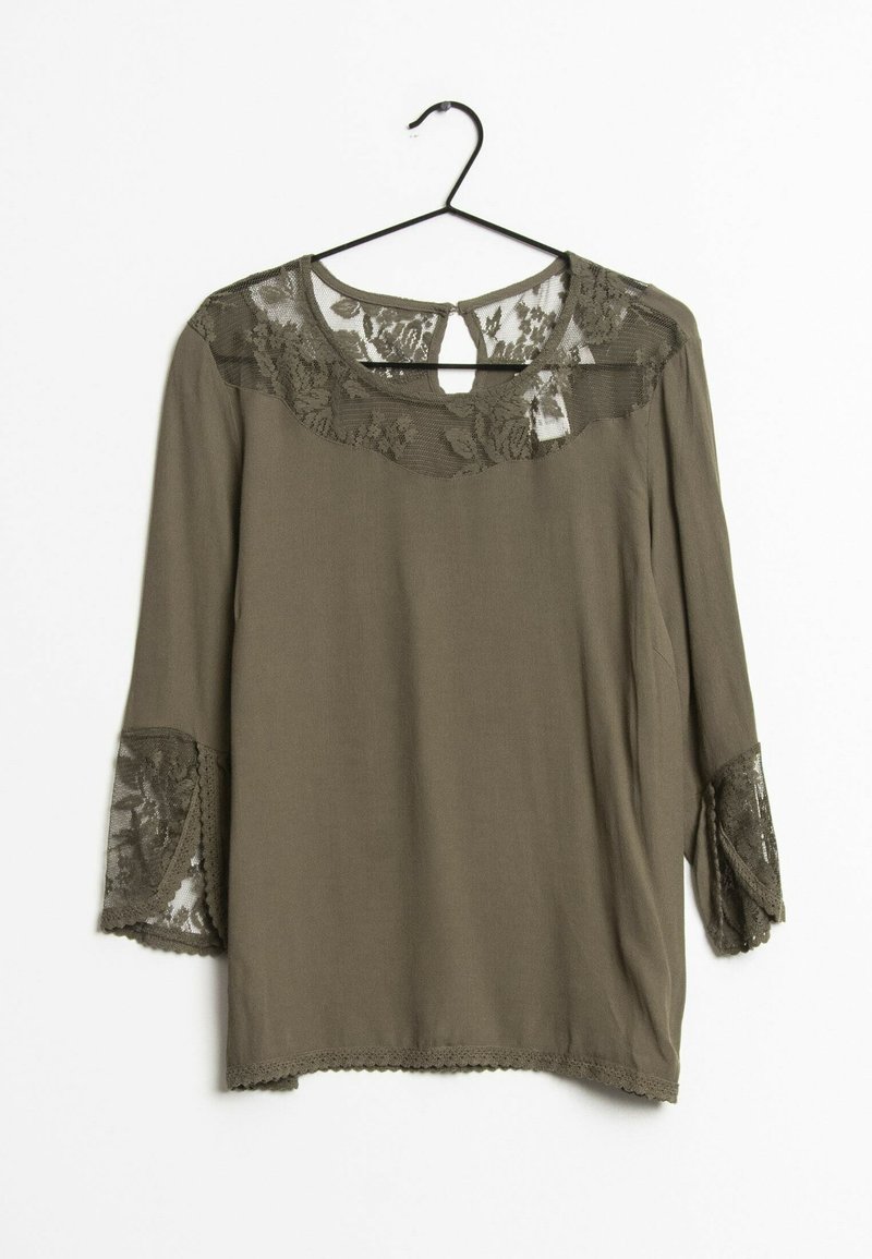 Blouse vert olive à manches longues avec de la dentelle florale sur les épaules, le haut de la poitrine et les poignets, suspendue à un cintre noir sur fond blanc.