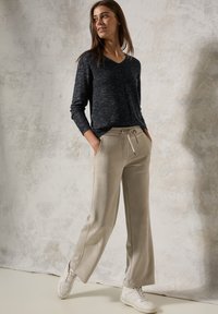 Schwarzes langärmliges V-Ausschnitt-Oberteil mit subtiler Streifenstruktur, kombiniert mit beige weit geschnittenen Hosen mit elastischem Bund und Taschen. Weiße Sneaker.