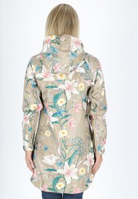 Beige regnrock med blommönster och huva, prydd med rosa liljor och blå blommor, långa ärmar och justerbara cuffs.