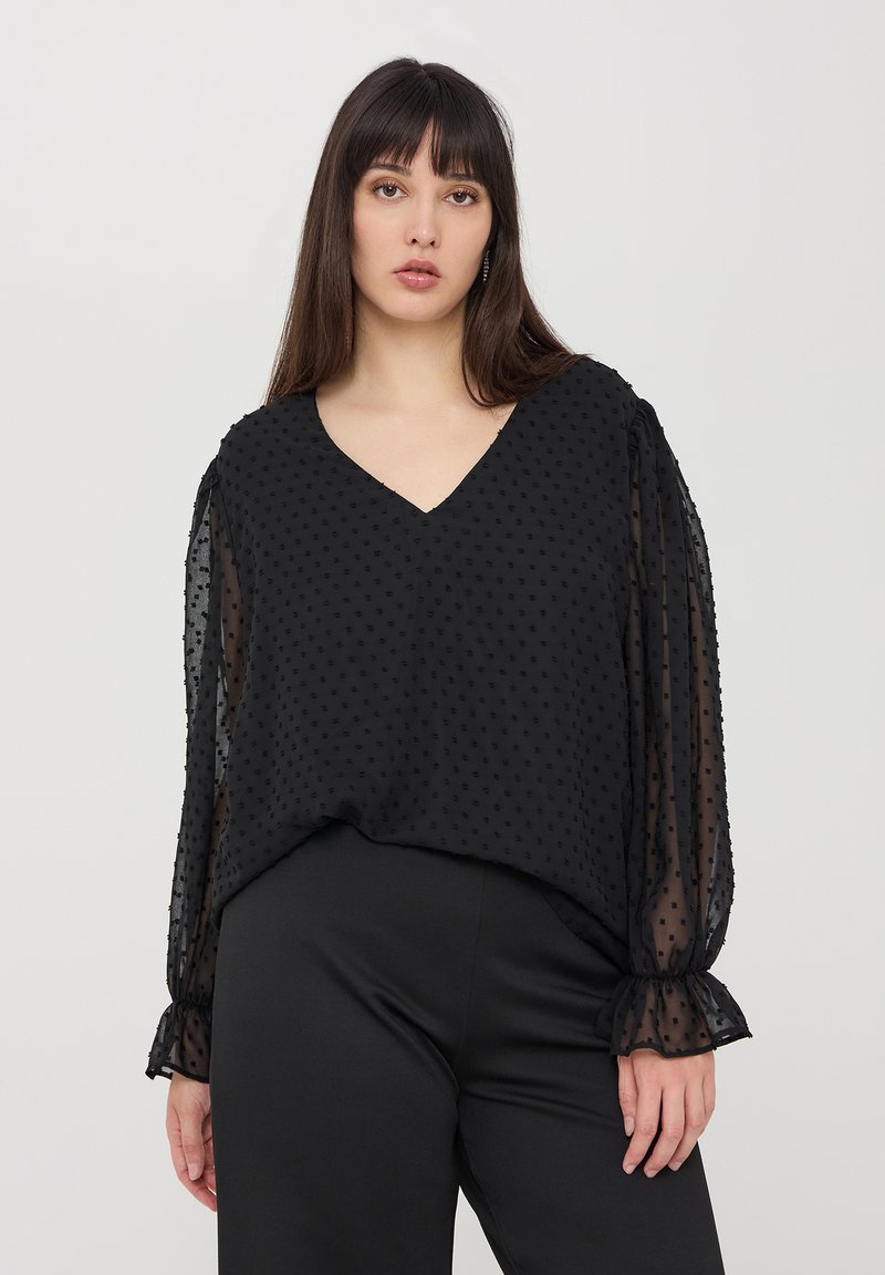 Blusa nera con scollatura a V, caratterizzata da motivi a pois texture e maniche lunghe trasparenti. Il design presenta polsini arricciati e una vestibilità comoda.